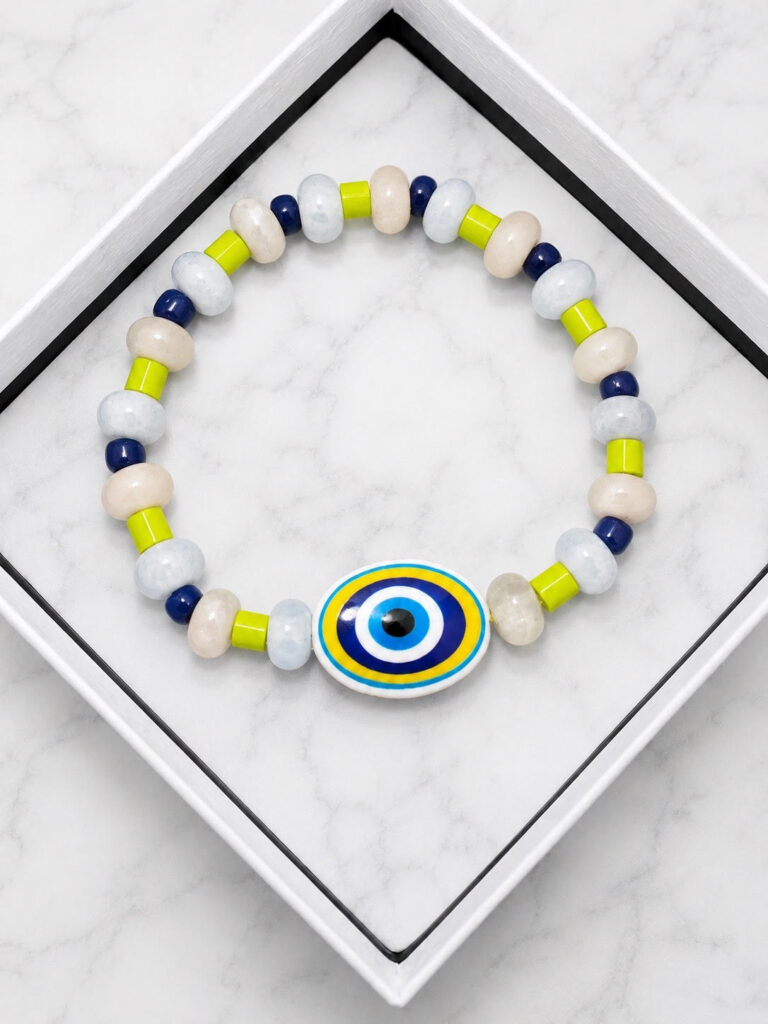 Handmade beaded bracelet with a large blue evil eye centerpiece, light blue and cream beads, navy accents, and bright chartreuse spacer beads displayed in a white jewelry tray.