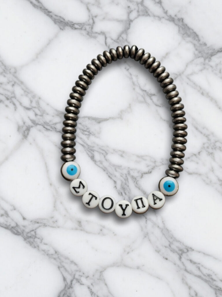 Handmade bracelet with silver-toned beads, Greek letter beads spelling “ΣΤΟΥΠΑ,” and blue evil eye accent beads displayed on a marble background.