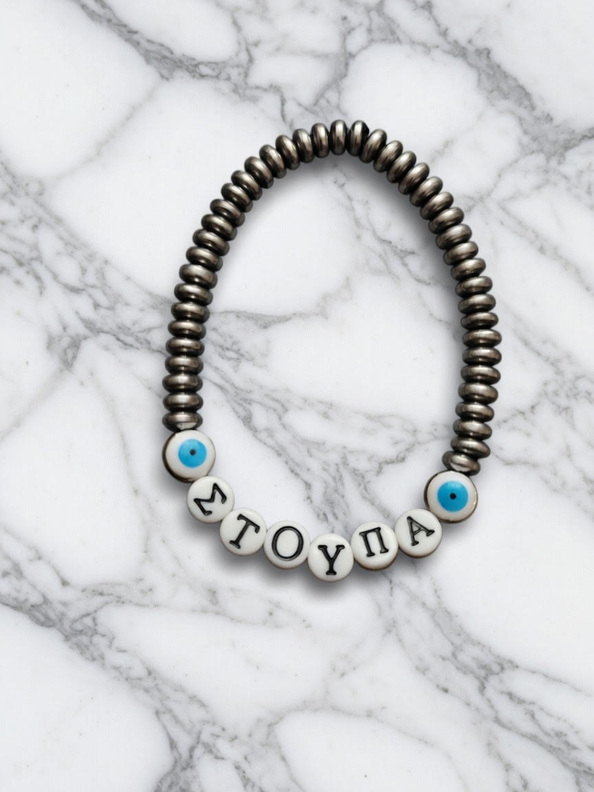 Handmade bracelet with silver-toned beads, Greek letter beads spelling “ΣΤΟΥΠΑ,” and blue evil eye accent beads displayed on a marble background.