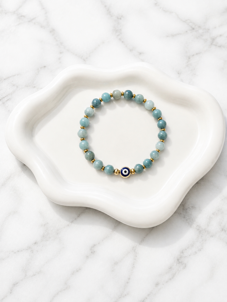 Handmade amazonite bead bracelet with gold spacer beads and a blue evil eye charm displayed on a white decorative tray.
